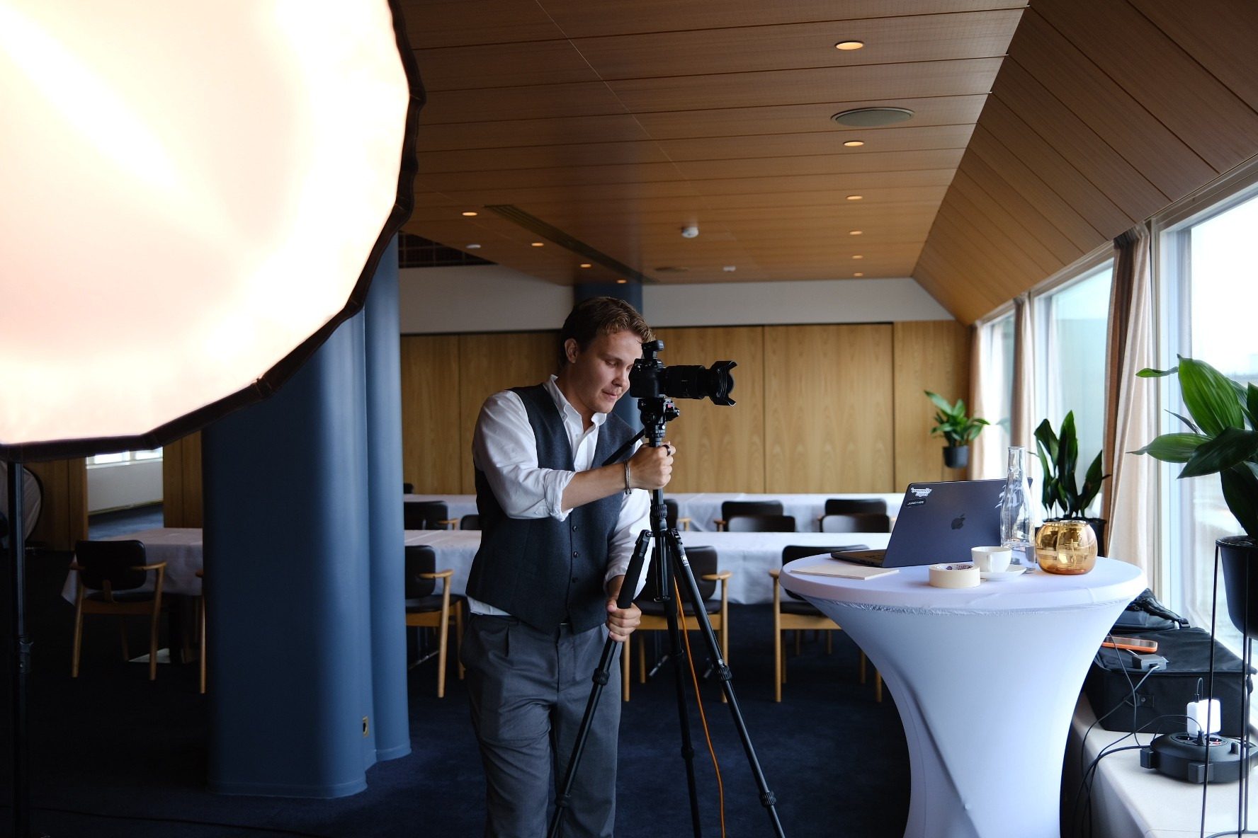 Lucas Ekblad framing a shot through the camera on a tripod, next to a high table with a laptop.